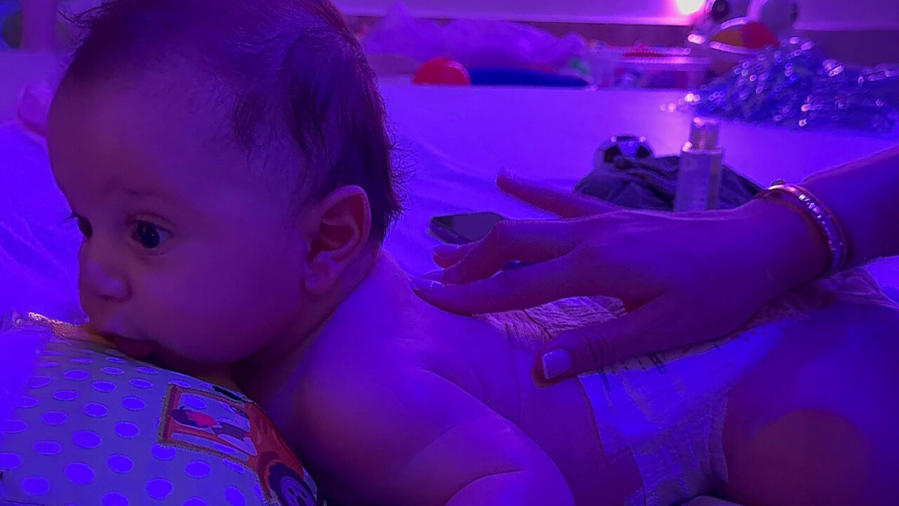A cozy baby on a bed, bathed in calming purple light.
