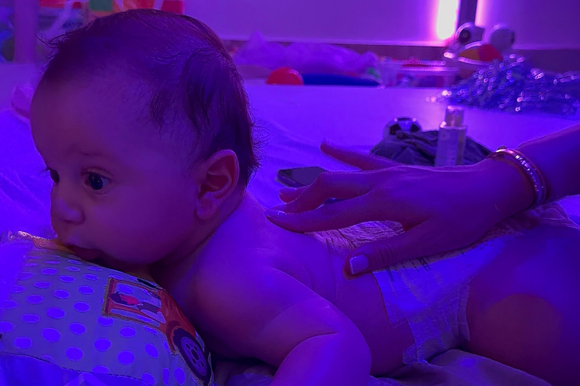 A cozy baby on a bed, bathed in calming purple light.
