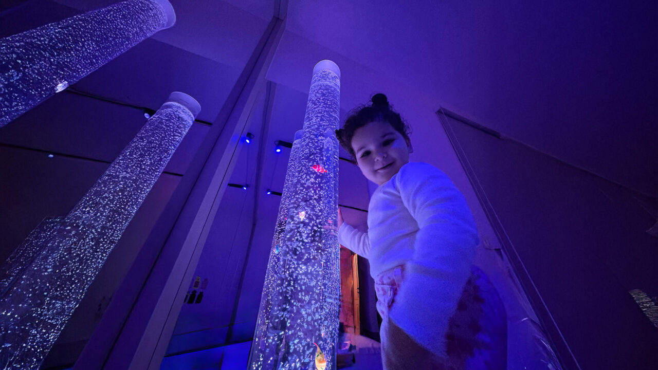 A young girl stands happily in front of a dazzling array of bright lights.