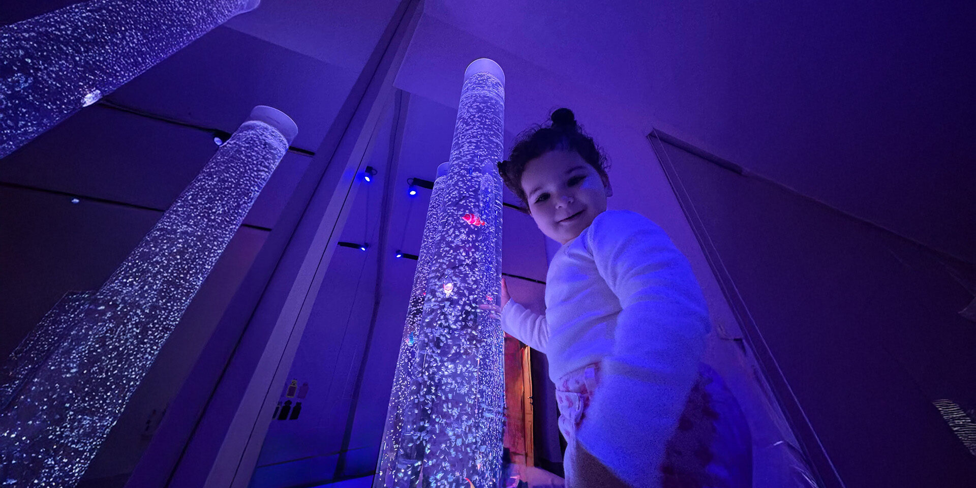 A young girl stands happily in front of a dazzling array of bright lights.