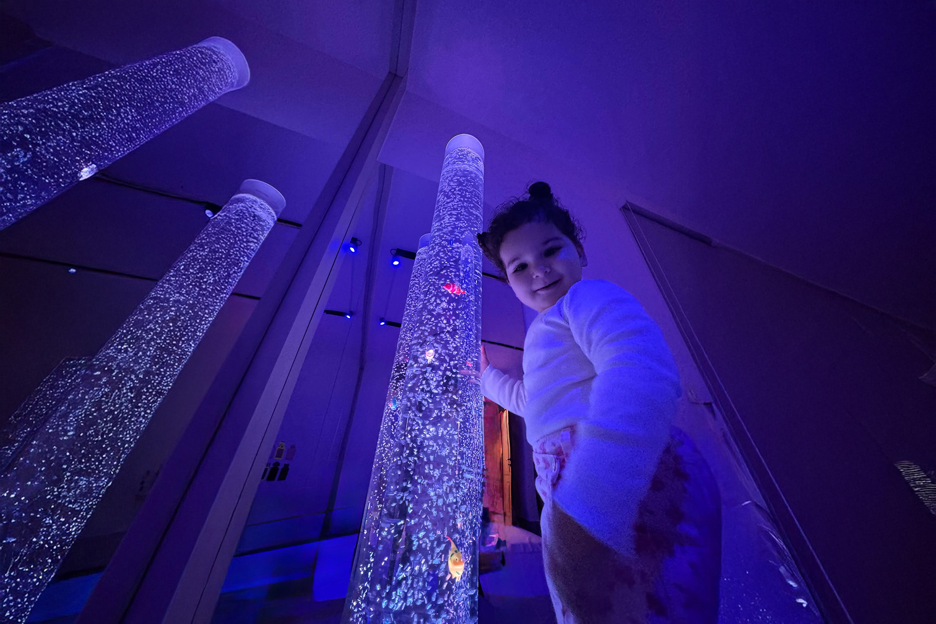 A young girl stands happily in front of a dazzling array of bright lights.